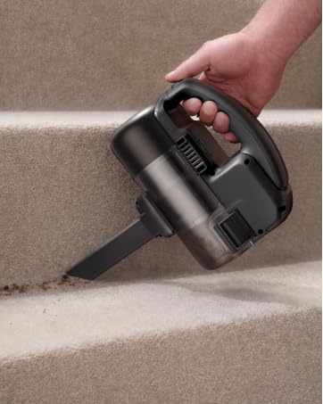 Handstaubsauger, der auf Teppichtreppen verwendet wird. Dunkelgraues Gerät mit Griff und Düse, die während des Betriebs sichtbar sind
