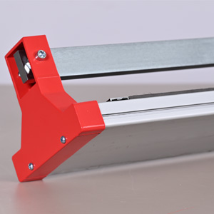 Close-up of a red and silver paper cutter or trimmer. The device features a long metal cutting blade and a red plastic handle for precision cutting.