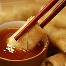 Chop sticks holding a spring roll dipping into Asian Organics Sweet Chili Sauce in a serving cup.