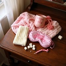 Craft or hobby scene featuring pink yarn, white knitting needles, and small white pom-poms on dark wooden surface. Shows knitting or crafting supplies.
