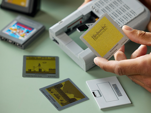 Multiple vintage Nintendo Game Boy cartridges spread on green surface, with hands inserting yellow cartridge into cleaning device.