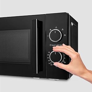 Black microwave oven with manual control dials. A hand adjusts the lower dial, demonstrating the manual operation of the appliance.