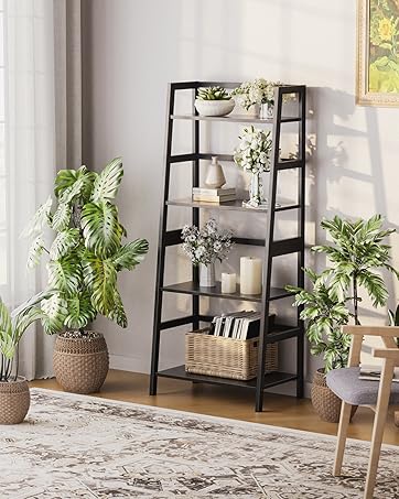 Modern ladder-style black shelving unit with five tiers, styled with plants, books and decorative items. Shown in bright interior setting with area rug and wooden chair.
