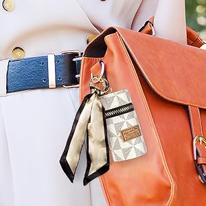 Close-up of an orange leather handbag with attached blue leather belt. A patterned keychain and scarf accessorize the bag.