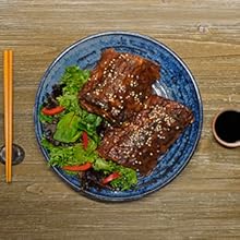 Asian barbeque baby back ribs on a blue plate with fresh greens and chop sticks on the side.