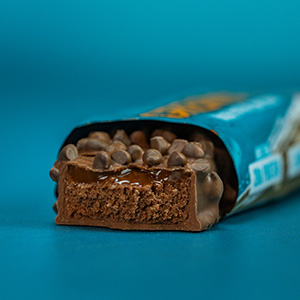 A chocolate protein or snack bar being unwrapped against a bright turquoise blue background.