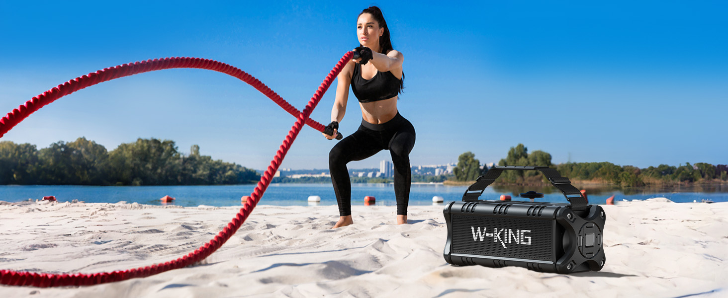 Red battle ropes and black exercise duffel bag on beach sand by water. Training equipment setup against natural backdrop.