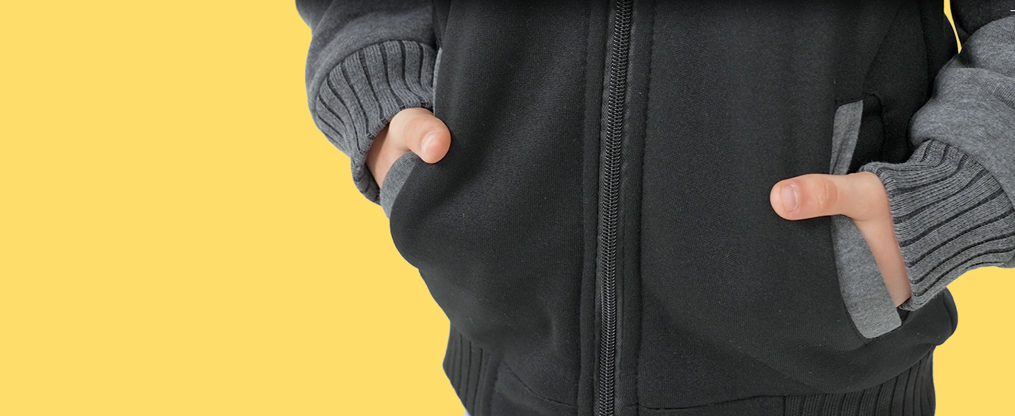 Nahaufnahme der Hände einer Person in den Taschen einer dunkelgrauen Jacke mit Reißverschluss und gerippten Bündchen, die die praktischen Eigenschaften des Kleidungsstücks zur Geltung bringt