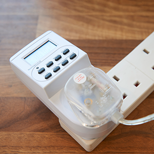 Digital timer device plugged into a power strip on a wooden surface, with a small clear container attached to its side.