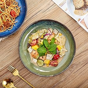 Two dishes on a wooden table: one with pasta and the other with a colorful salad containing vegetables, herbs, and cubed ingredients.