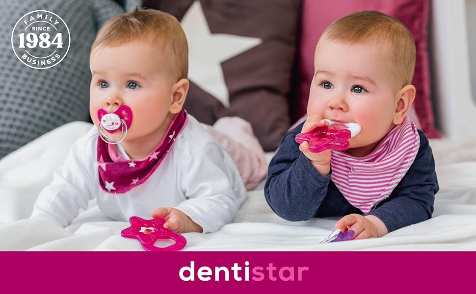 Two infants wearing bandana-style bibs, with pink teething accessories, positioned on soft furniture. Dentistar branding visible at bottom.