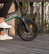 Vista parcial de una rueda de bicicleta y las piernas de una persona en una plataforma de madera. La imagen se centra en la parte inferior de la escena.