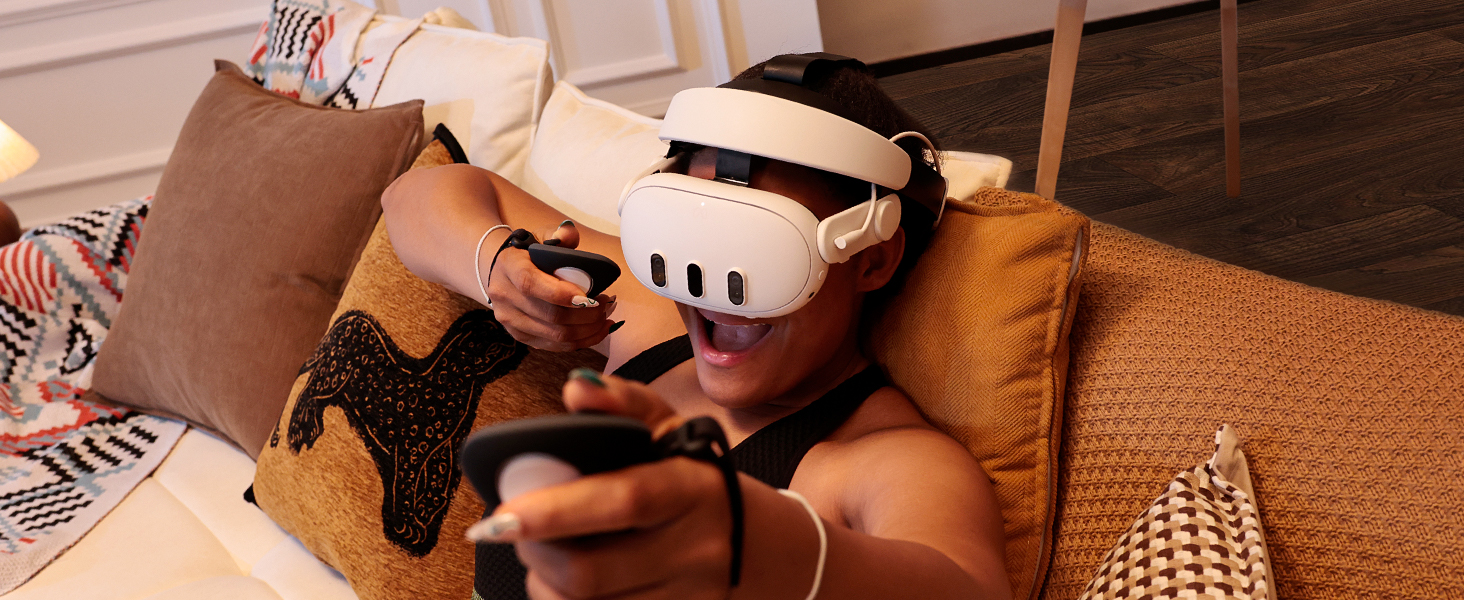 Personne utilisant un casque de réalité virtuelle assise sur un canapé brun, tenant des manettes de jeu.