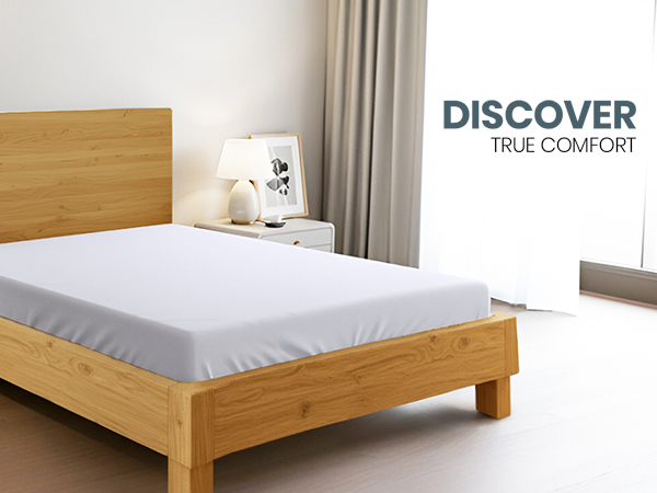 Wooden bed frame with white mattress in minimalist bedroom. Light wood headboard and legs. White bedding and neutral decor elements visible.