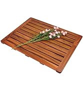 Wooden bath mat with slatted design, featuring parallel strips of wood. Small pink flowers rest on top, highlighting its use in bathroom settings.