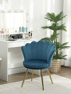 Fauteuil d'appoint à dossier en velours bleu sarcelle avec pieds en métal doré dans une pièce d'un blanc éclatant avec vanité et plantes en pot.