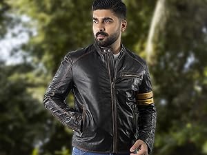 Dunkelbraune Lederjacke mit Used-Finish, Frontreißverschluss, Stehkragen, Brusttasche und gelber Armbinde. Wird im Freien vor verschwommenem grünem Hintergrund getragen