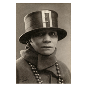Sepia photograph of a woman in a top hat with a large buckle. She is wearing necklaces with beads.