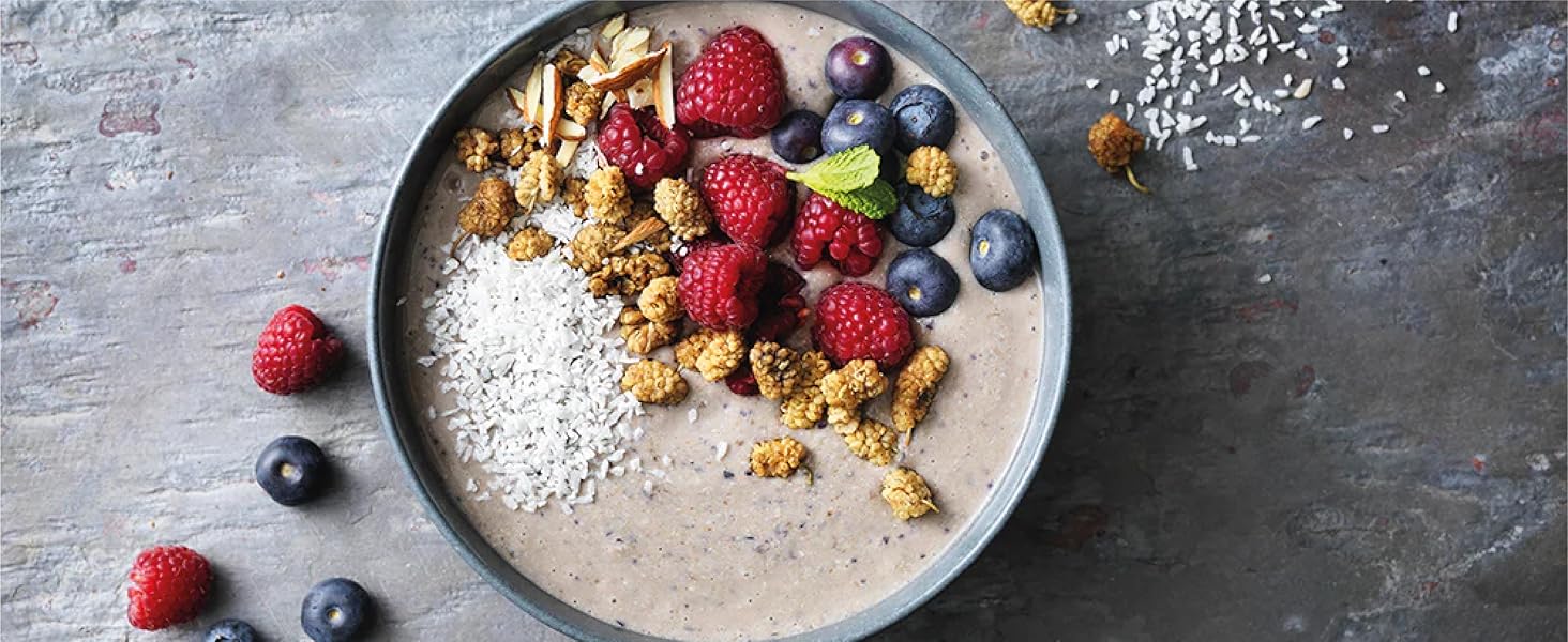 Bowl of smoothie topped with granola, fresh berries, and chia seeds. Raspberries, blueberries, and granola scattered around the bowl.