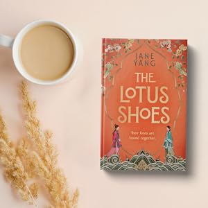 Orange hardback book next to a cup of tea and dried plants on pink background