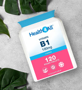 White bottle of vitamin B1 supplements. Label shows 120 tablets, 100mg dosage. Green leaves and blue fabric in background.