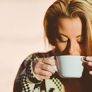 Lifestyle-Foto in warmen Tönen, das jemanden zeigt, der eine weiße Kaffeetasse oder einen Becher in der Hand hält und daraus trinkt.