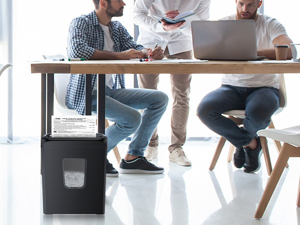 Under-desk footrest in dark color. People sitting at table with laptops, footrest visible beneath. Designed for ergonomic support in office settings.