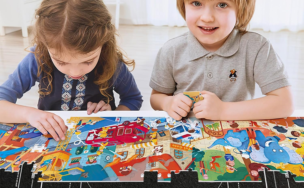 Children assembling a colorful jigsaw puzzle featuring cartoon characters, buildings, and animals. The large puzzle pieces are spread out on a table.