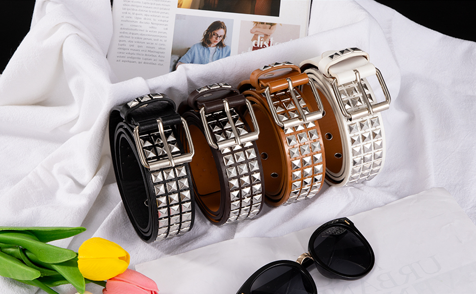Quattro collari o braccialetti in pelle disposti su tessuto bianco, con borchie decorative in metallo e chiusure con fibbia in diverse tonalità di marrone e