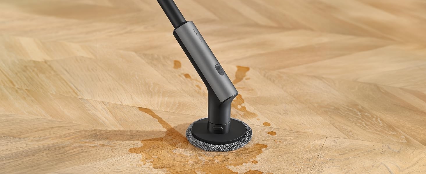Black handheld steam cleaner head with circular brush attachment pressing against a tan surface, producing visible steam.