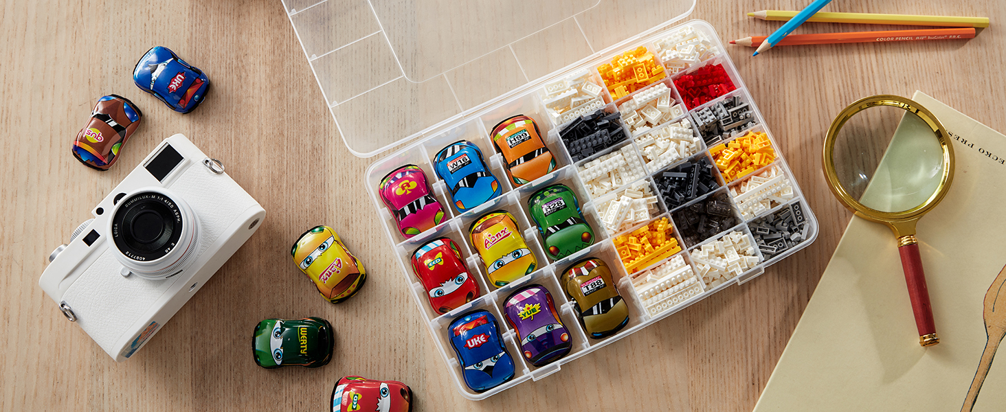Tischszene mit bunten Spielzeugautos in einem durchsichtigen Kunststoff-Organizer, dazu eine weiße Kamera, eine Lupe und Farbstifte
