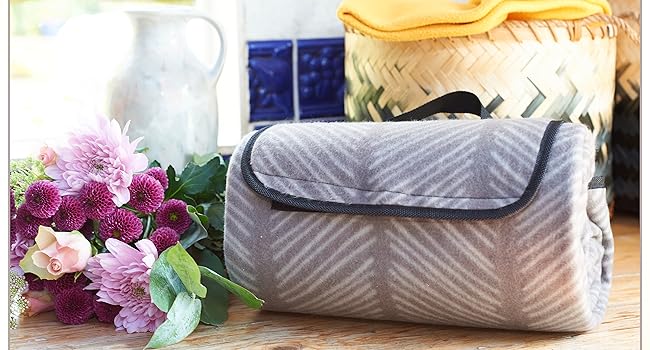 Grey quilted travel mat with carry handle, shown with wicker basket and flowers. Product features include wipe-dry capability and quick-drying without fading.