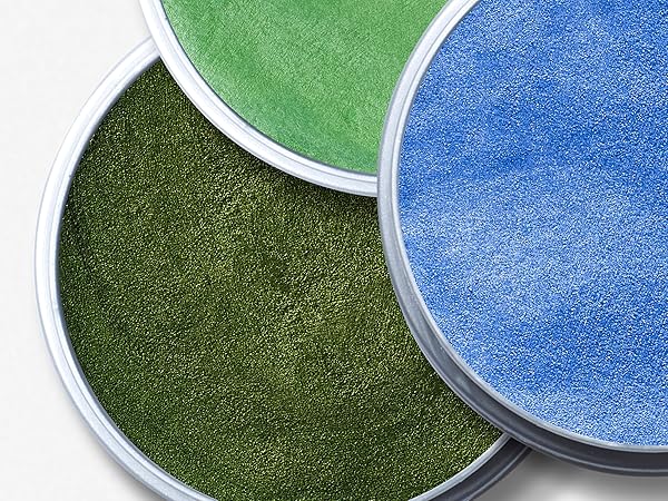 Close-up of three round makeup or face paint pans in different shades of green and blue, showing metallic sheen and pressed powder texture.