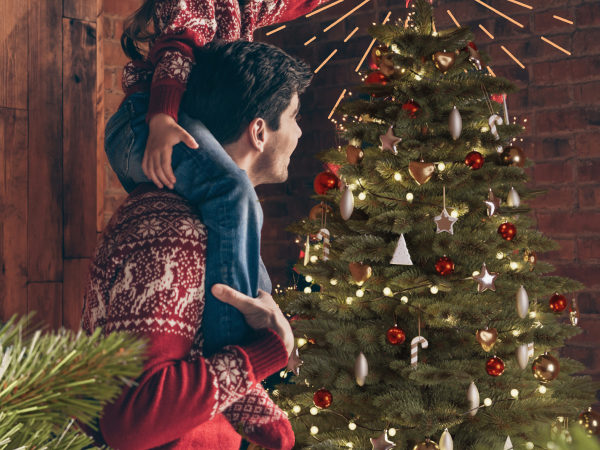 Gemütliche Weihnachtsszene mit einem geschmückten Weihnachtsbaum mit roten Ornamenten, Lichtern und traditionellen Dekorationen in einem warm beleuchteten Raum.