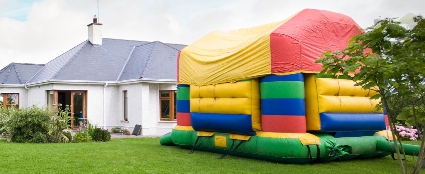 Grande casetta gonfiabile o percorso a ostacoli allestito su un prato verde all'esterno di una casa residenziale bianca. Presenta vivaci sezioni di colore rosso, giallo, blu
