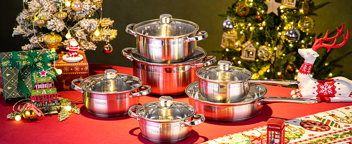 Set of stainless steel cookware with glass lids on red tablecloth. Christmas decorations and gift boxes in background.