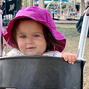 cute girl in purple hat smiling while on a swing