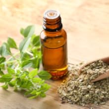 Essential oil bottles with fresh green herbs and leaves arranged on wooden surface, showing natural ingredient composition.