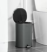 Gray cylindrical pedal trash can with black lid, shown open in bathroom setting next to white toilet. Features a sleek, modern design with foot pedal operation.