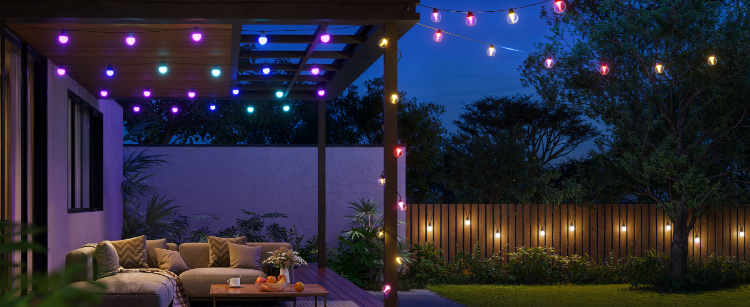 Outdoor patio setting at dusk with string lights creating ambient lighting across a covered seating area. Modern lounge furniture visible beneath pergola with wooden privacy fence in background.