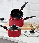 Multiple pans and cookware displayed on textured counter surface, including red and black pans with visible handles.