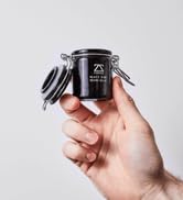 Hand holding a small black canister with a metal locking lid. The container has '24' printed on it in white text.