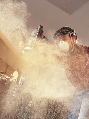 A cloud of wood dust forms from a man using a power sander on a table edge