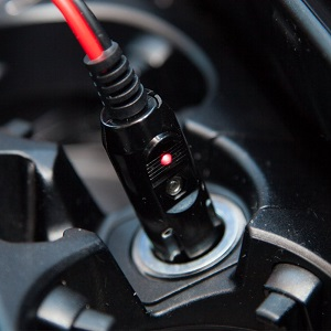 Close-up of car charging port with red and black cable connector, showing illuminated LED indicator.