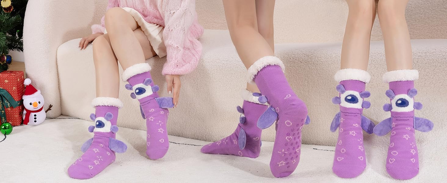 Multiple views of fuzzy purple socks with cartoon-style eye designs, displayed on feet against light backgrounds.