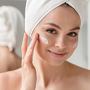 Junge schöne Frau schmiert Creme auf ihr Gesicht
