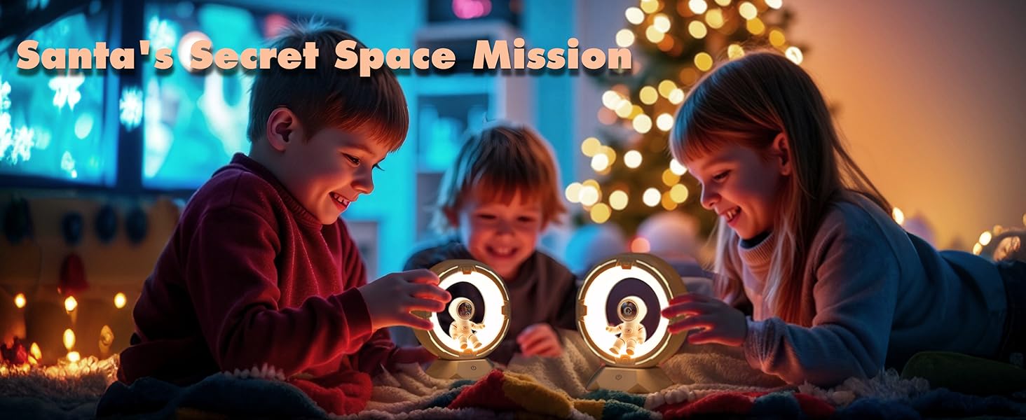 Three children gathered around two illuminated space-themed devices with astronaut figures inside. Christmas tree and decorative lights visible in background.