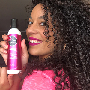 Girl with curly hair, holding pink product bottle, looking at you from the left.