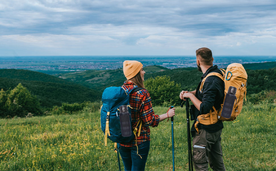 De excursionistas con mochilas grandes que contemplan un vasto paisaje desde la cima de una colina. Traigan ropa para actividades al aire libre y bastones de senderismo.