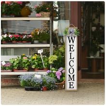 Storefront with &#34;WELCOME&#34; sign, colorful potted flowers, and price tags on shelves.